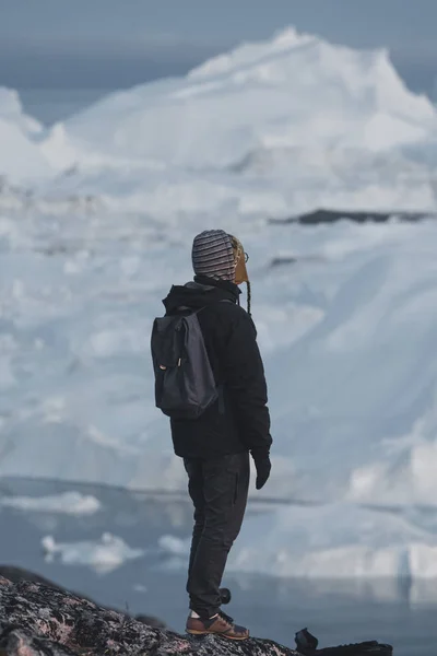 Grönländsk turist utforskare med utsikt över isfjorden i Ilulissat. Res i arktiskt landskap natur med isberg. Turistperson som tittar på fantastisk utsikt över Grönlands isfjorden. Människa vid is och isberg — Stockfoto