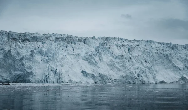 Zamknij ujęcie ogromnej ściany lodowca. Duże kawałki lodu odłamują się. Nastrojowa i pochmurna pogoda. Lodowiec Eqip Sermia nazywany lodowcem Eqi. Grenlandzkie topnienie pokrywy lodowej z powodu globalnego ocieplenia. — Zdjęcie stockowe