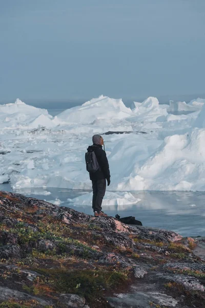 Гренландський туристичний дослідник з видом на Ілефіорд в Ілуліссаті. Подорож в арктичному ландшафті з айсбергами. Туристична людина дивиться на унікальний краєвид гренландського айсфеорду. Людина за льодом і айсбергом — стокове фото