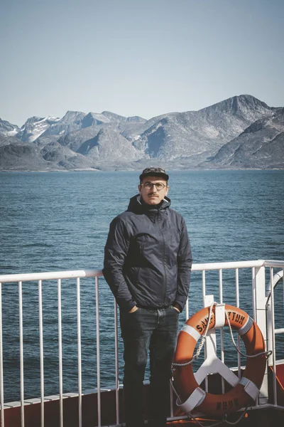 Joven guapo mirando hacia adelante y sonriendo mientras está de pie en la cubierta de un barco en el Ártico. A bordo del buque costero Sarfaq Ittuk en Groenlandia que viaja de Ilulissat a Nuuk . —  Fotos de Stock