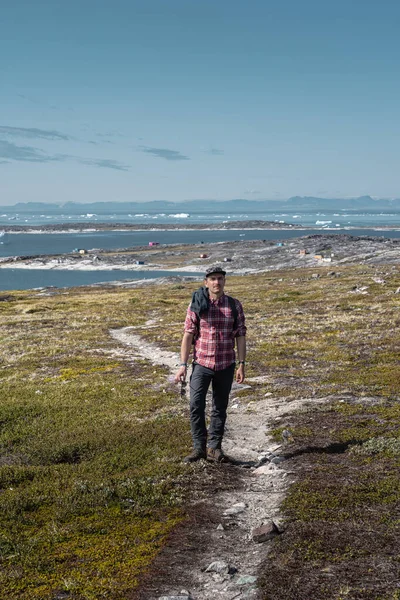 Jongeman toerist voor de ijsberg. Uitzicht op Icefjord in Ilulissat. IJsbergen van Kangia gletsjer in Groenland zwemmen met blauwe lucht en wolken. Symbool van opwarming van de aarde. — Stockfoto