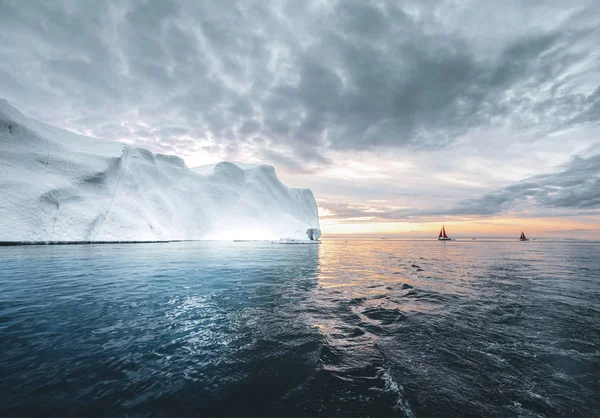 美丽的红色帆船在北极旁边巨大的冰山显示规模。在迪斯科湾冰川的浮冰山之间巡航，在极夏伊卢利萨的午夜太阳季节，迪斯科湾 — 图库照片