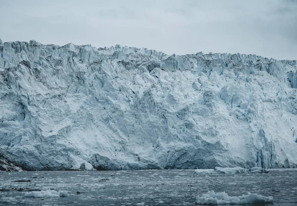 Nahaufnahme einer riesigen Gletscherwand. Große Eisbrocken brechen ab. launisches und bewölktes Wetter. eqip sermia glacier genannt eqi glacier. Schmelze der grönländischen Eiskappen aufgrund der globalen Erwärmung. — Stockfoto