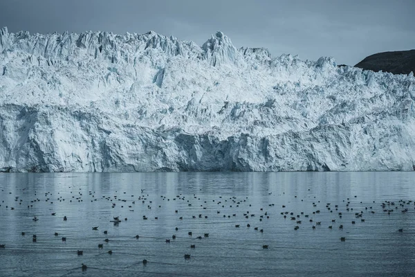 Nahaufnahme einer riesigen Gletscherwand. Große Eisbrocken brechen ab. launisches und bewölktes Wetter. eqip sermia glacier genannt eqi glacier. Schmelze der grönländischen Eiskappen aufgrund der globalen Erwärmung. — Stockfoto