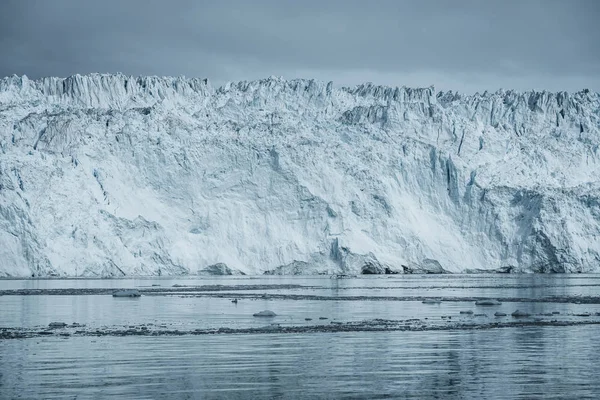 Nahaufnahme einer riesigen Gletscherwand. Große Eisbrocken brechen ab. launisches und bewölktes Wetter. eqip sermia glacier genannt eqi glacier. Schmelze der grönländischen Eiskappen aufgrund der globalen Erwärmung. — Stockfoto