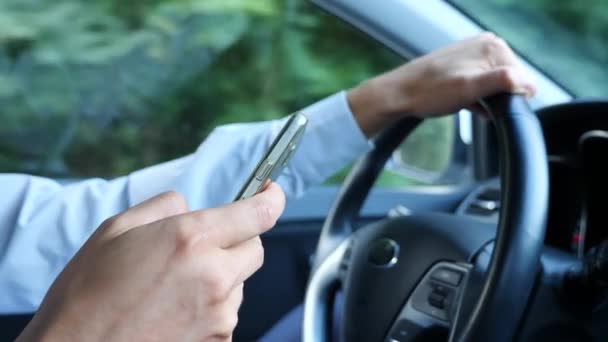 手とステアリング ホイール。男性ビジネスマンは車を運転して、彼の携帯電話にメッセージを参照します。交通ルールの違反。4 k、スローモーション — ストック動画