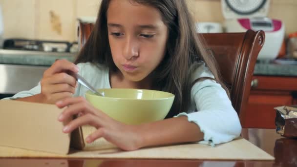 Una niña de 8-10 años come cereales de desayuno con leche en una mesa en la cocina y mira en su teléfono inteligente. 4k, cámara lenta — Vídeos de Stock