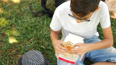 Çekici çocuk çim Park'ta bir ağacın altında oturup taze hamburger yeme. 4k, ağır çekim