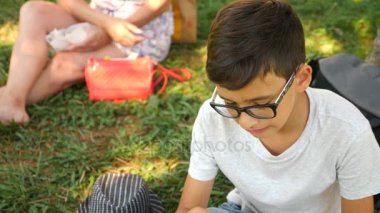 Çekici çocuk çim Park'ta bir ağacın altında oturup taze hamburger yeme. 4k, ağır çekim