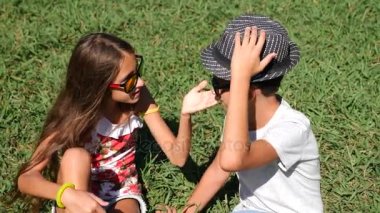 erkek ve kız, 10-12 yaşında ikiz güneşli bir yaz parkta bir açıklıkta oturuyor. sevinirler ve kucaklamak. 4k, yakın çekim, yavaş hareket, kopya alanı