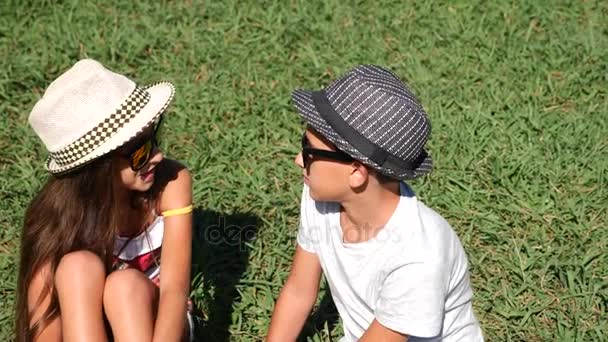 Ragazzo e ragazza, gemelli 10 - 12 anni sono seduti in una radura nel parco in una giornata di sole estivo. gioire e abbracciare. 4k, primo piano, rallentatore, spazio di copia — Video Stock