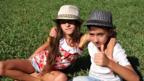 Menino e menina, gêmeos 10 - 12 anos de idade estão sentados em uma clareira no parque em um dia ensolarado de verão. regozijai-vos e abraçai. 4k, close-up, câmera lenta, espaço de cópia — Vídeo de Stock