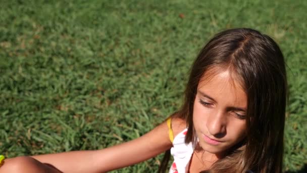 Una niña de 10 años se sienta en un prado verde en un día soleado de verano. Primer plano. En cámara lenta. 4k — Vídeo de stock