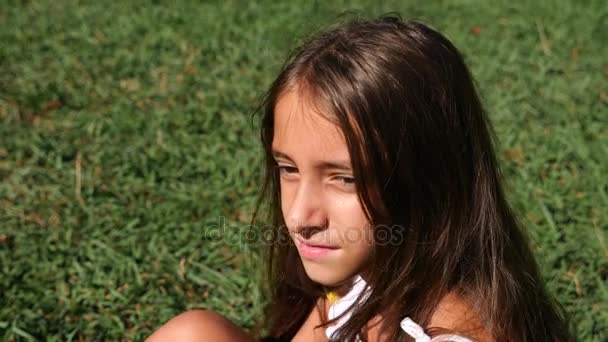 Uma menina, 10 anos, senta-se em um prado verde em um dia ensolarado de verão. close-up. Movimento lento. 4k — Vídeo de Stock