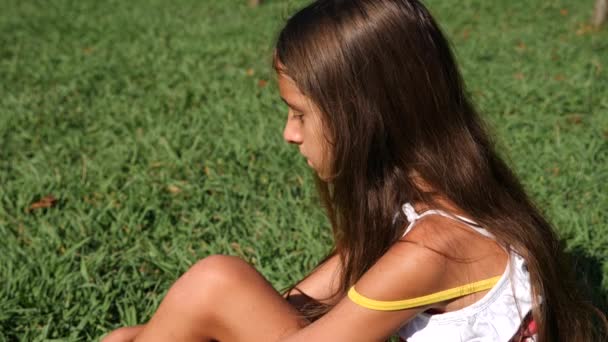 Dziewczynka, lat 10, siedzi na zielonej łące w słoneczny letni dzień. szczelnie-do góry. Zwolnionym tempie. 4k — Wideo stockowe