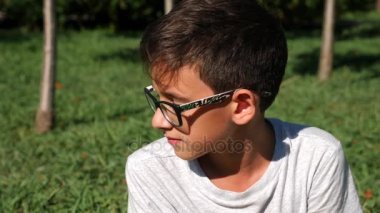 Çocuk 12 yaşında oturur bir yeşil çayır üzerinde yaz güneşli bir günde. yakın çekim. Ağır çekim. 4k