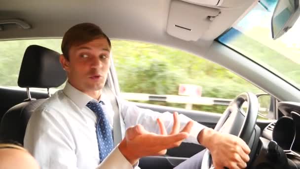 Мужчина-бизнесмен в рубашке и галстуке разговаривает с пассажиром, отвлекаясь от дороги. нарушение правил дорожного движения. 4k, slow motion — стоковое видео