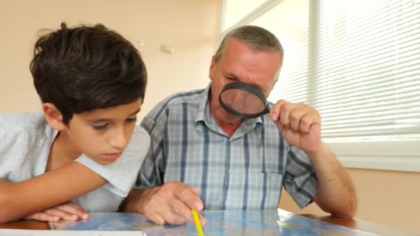 Hombre mayor mirando el mapa con nieto a través de la lupa de la casa en la oficina, estilo de vida, 4k, cámara lenta — Vídeos de Stock