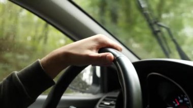 Yağmurda arabada ön cam yoldan görünümünü. Su damlaları görüntülemek zorlaştırır camına düşüyor. 4k, ağır çekim. adam direksiyon tutan.