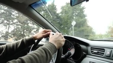 Yağmurda arabada ön cam yoldan görünümünü. Su damlaları görüntülemek zorlaştırır camına düşüyor. 4k, ağır çekim. adam direksiyon tutan.