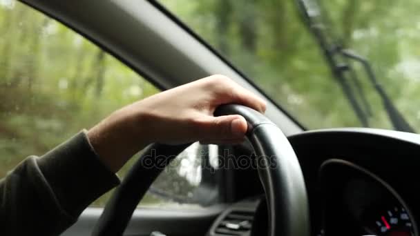 Vista de la carretera desde el parabrisas del coche bajo la lluvia. Gotas de agua caen sobre el vaso, por lo que es difícil de ver. 4k, cámara lenta. el hombre sostiene el volante . — Vídeo de stock