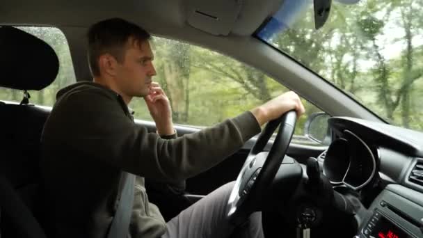 Vue sur la route depuis le pare-brise de la voiture sous la pluie. Des gouttes d'eau tombent sur le verre, ce qui le rend difficile à voir. 4k, au ralenti. l'homme tient le volant . — Video