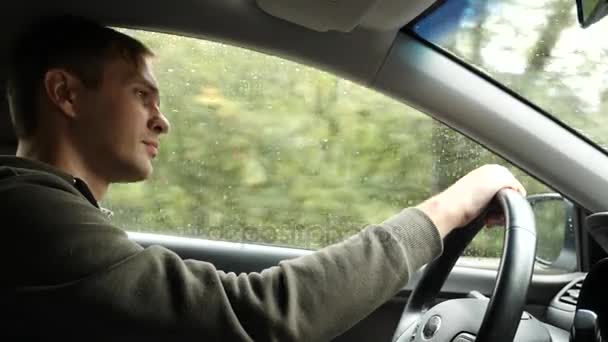 Vue sur la route depuis le pare-brise de la voiture sous la pluie. Des gouttes d'eau tombent sur le verre, ce qui le rend difficile à voir. 4k, au ralenti. l'homme tient le volant . — Video