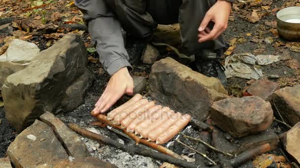 Mand madlavning pølser på en camping brand. Turist stegte pølser i det fri. 4k – Stock-video