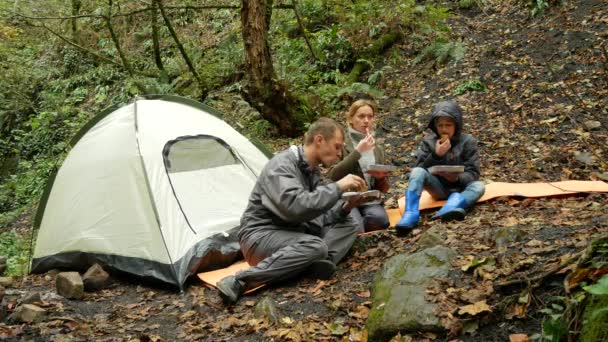 Family, mom, dad and son is eating grilled sausages outdoors in a tourist camp. 4k, — Stock Video