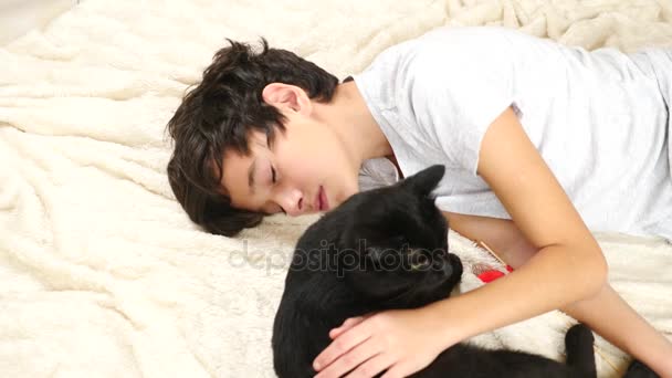 O menino abraça e acaricia seu animal de estimação, um gato preto. 4k, câmera lenta — Vídeo de Stock