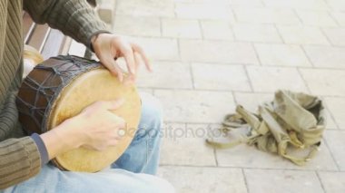 Bir sokak müzisyen bir Afrika davul çalıyor. Bongo davulunun üstündeki oynayan adam. yakın çekim. Bongo dokunarak el davul. 4k, ağır çekim çekim. Güneş parlamak.