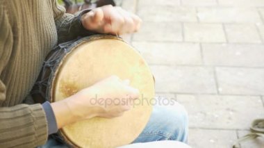 Bir sokak müzisyen bir Afrika davul çalıyor. Bongo davulunun üstündeki oynayan adam. yakın çekim. Bongo dokunarak el davul. 4k, ağır çekim çekim. Güneş parlamak.