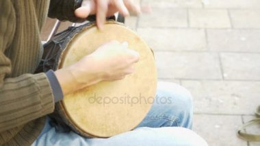 Bir sokak müzisyen bir Afrika davul çalıyor. Bongo davulunun üstündeki oynayan adam. yakın çekim. Bongo dokunarak el davul. 4k, ağır çekim çekim. Güneş parlamak.