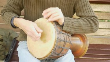 Bir sokak müzisyen bir Afrika davul çalıyor. Bongo davulunun üstündeki oynayan adam. yakın çekim. Bongo dokunarak el davul. 4k, ağır çekim çekim. Güneş parlamak.
