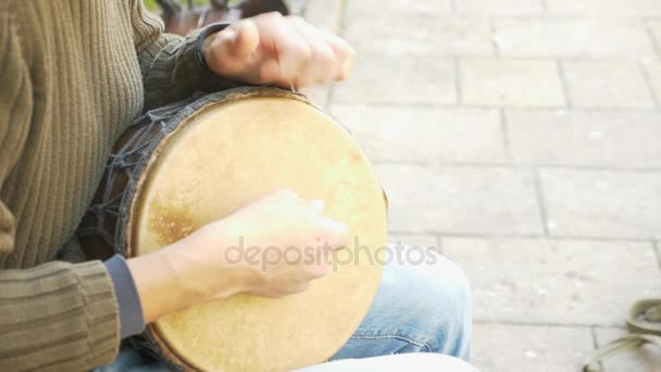 Um músico de rua toca num tambor africano. Um homem a tocar num tambor Bongo. Fecha. Mão tocando um tambor Bongo. 4K, tiro em câmara lenta. brilho do sol . — Vídeo de Stock