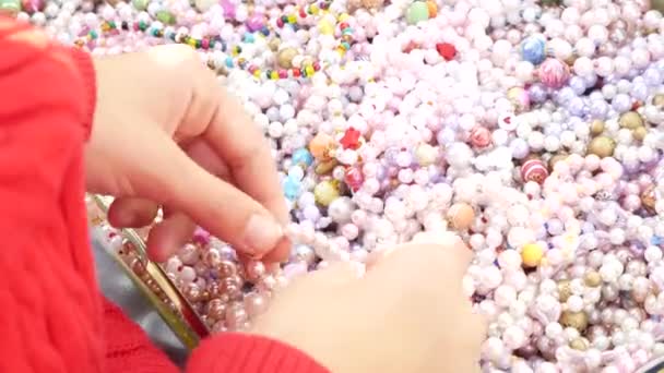 Una bambina sceglie braccialetti da perline di madreperla, li prova sul braccio. 4k, primo piano . — Video Stock