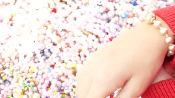 En liten flicka väljer armband från pärlemor pärlor, försöker dem på armen. 4k, närbild. — Stockvideo