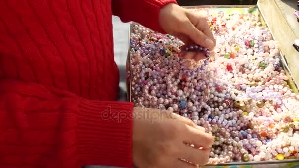 Una bambina sceglie braccialetti da perline di madreperla, li prova sul braccio. 4k, primo piano . — Video Stock