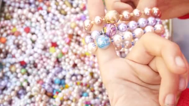 Ein kleines Mädchen sucht sich Armbänder aus Perlmutt-Perlen aus, probiert sie am Arm aus. 4k, Nahaufnahme. — Stockvideo