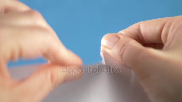 Hands tearing paper sheet, closeup on a turquoise background. 4k, slow motion — Stock Video