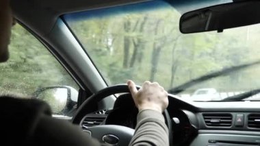 Yağmurda arabada ön cam yoldan görünümünü. Su damlaları görüntülemek zorlaştırır camına düşüyor. 4k, ağır çekim. adam direksiyon tutan.
