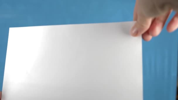 Manos de mujer sosteniendo un papel en blanco tamaño A5 o papel carta sobre un fondo turquesa. 4k, cámara lenta — Vídeos de Stock