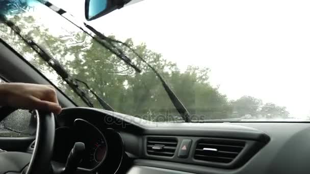 Vista de la carretera desde el parabrisas del coche bajo la lluvia. Gotas de agua caen sobre el vaso, por lo que es difícil de ver. 4k, cámara lenta. el hombre sostiene el volante . — Vídeo de stock