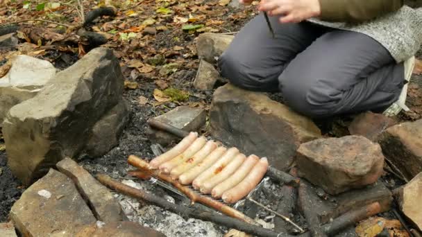 Mujer cocinando salchichas en una fogata. Embutidos fritos turísticos al aire libre. 4k — Vídeos de Stock