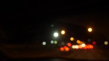 Gece araba sürüyorum. Şehirdeki bulanık arabalar. Şehrin caddelerinde bulanık trafiği olan aydınlatılmış ön araba penceresi. 4k
