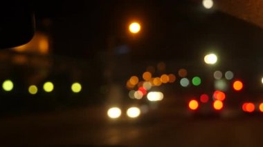 Gece araba sürüyorum. Şehirdeki bulanık arabalar. Şehrin caddelerinde bulanık trafiği olan aydınlatılmış ön araba penceresi. 4k