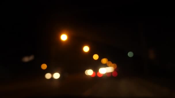 Gece araba sürüyorum. Şehirdeki bulanık arabalar. Şehrin caddelerinde bulanık trafiği olan aydınlatılmış ön araba penceresi. 4k — Stok video