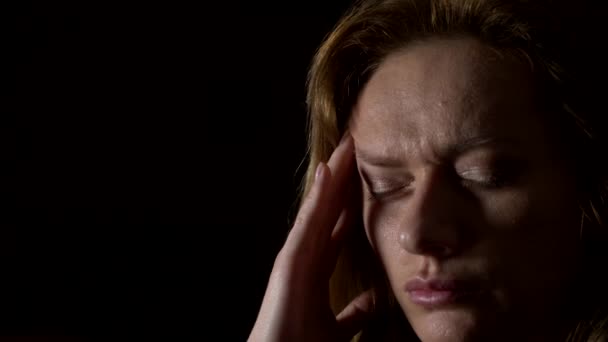 Nahaufnahme, traurige Frau mit Kopfschmerzen auf dunklem Hintergrund. 4k, Zeitlupe — Stockvideo