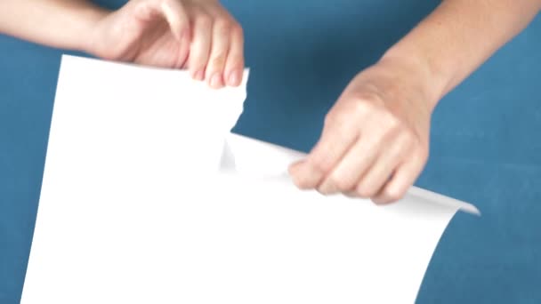 Manos rasgando hoja de papel, primer plano sobre un fondo turquesa. 4k, cámara lenta — Vídeo de stock