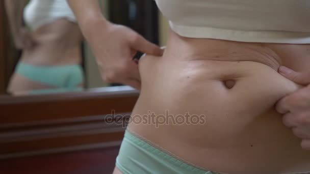 Расстроенная женщина, смотрящая в зеркало, касающаяся жира на животе. 4k, slow motion — стоковое видео